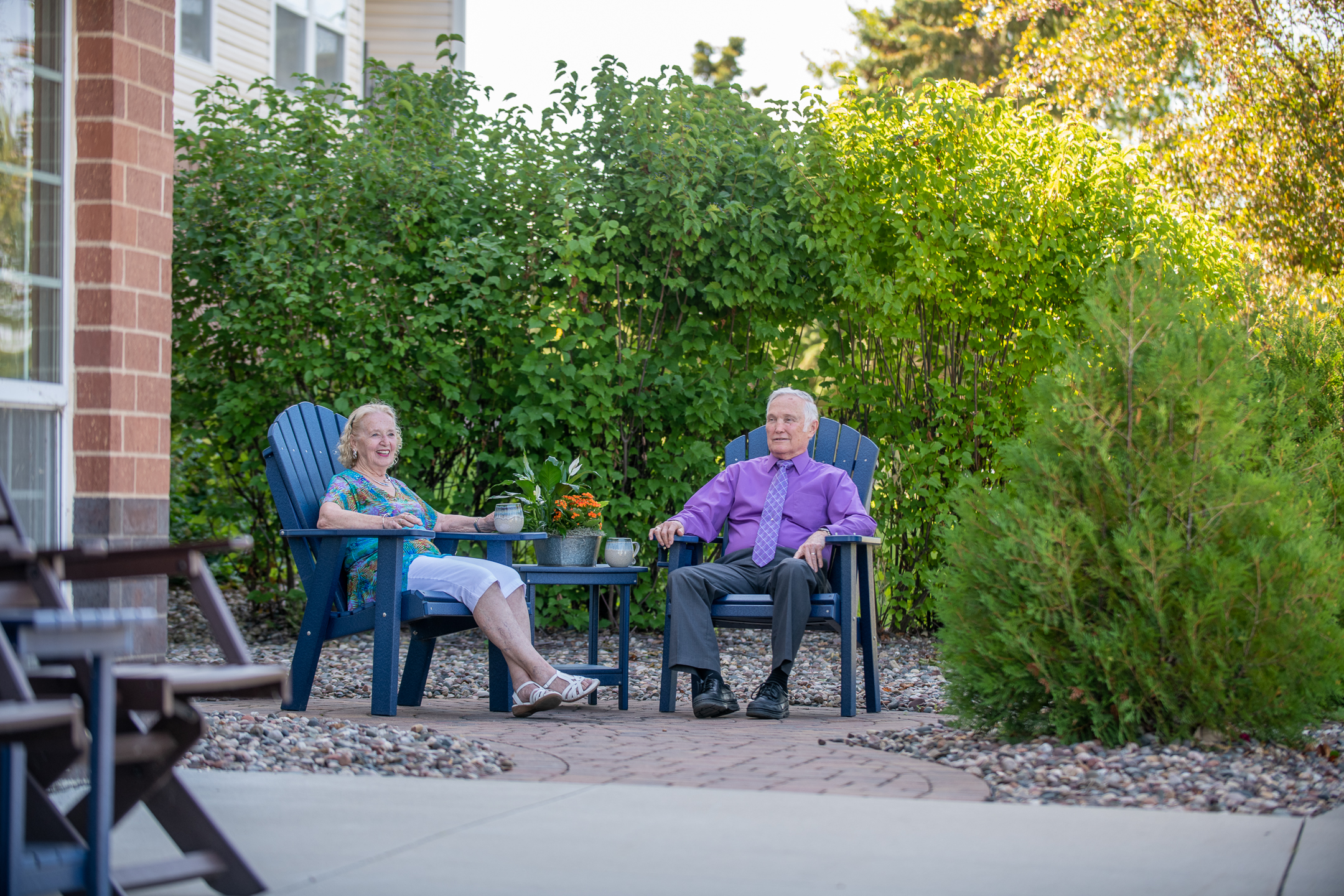 Seniors enjoying a sunny day on a patio surrounded by trees - independent senior living