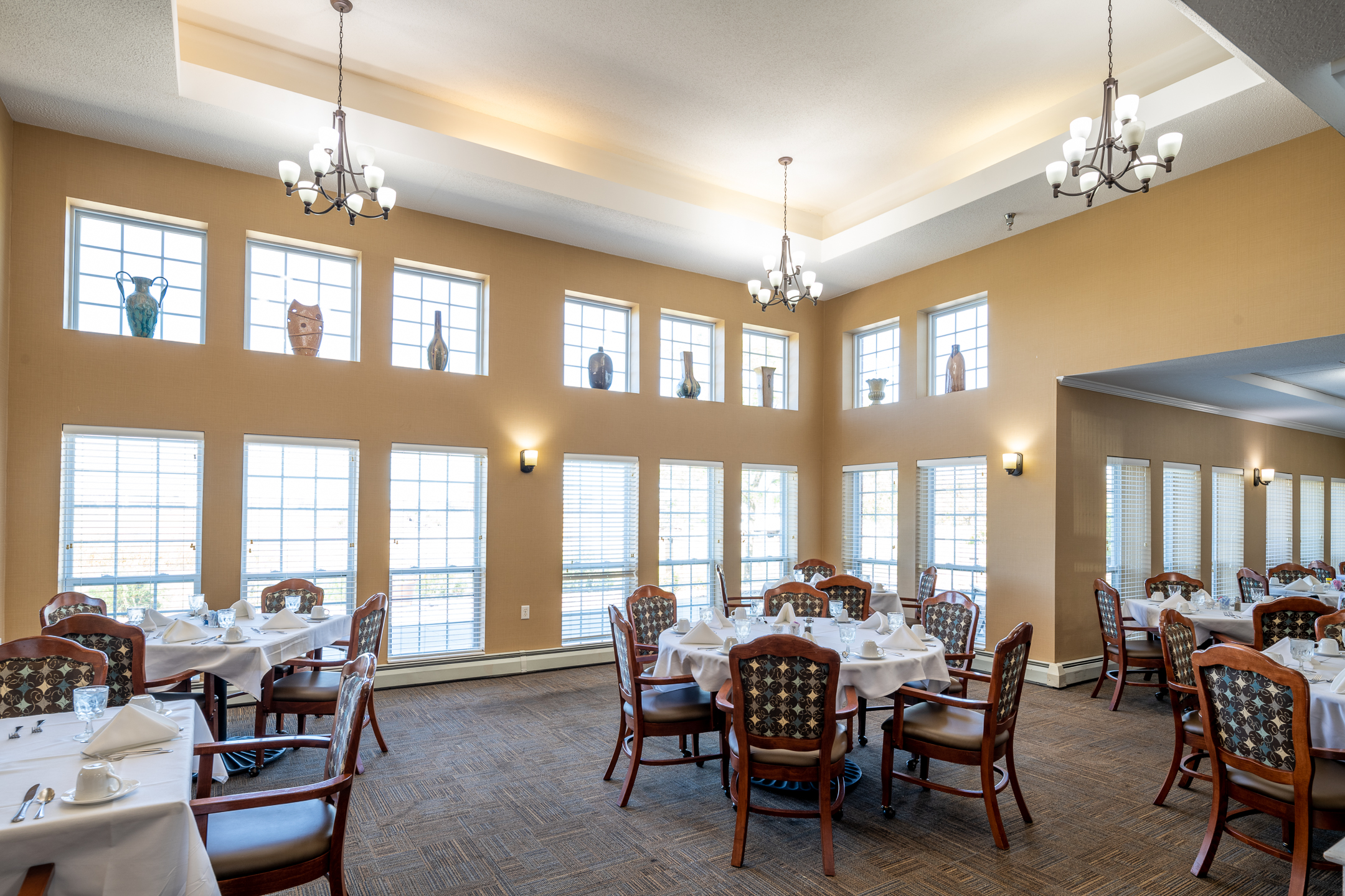Spacious living room in senior residence with tall windows and armchairs - senior living communities near me