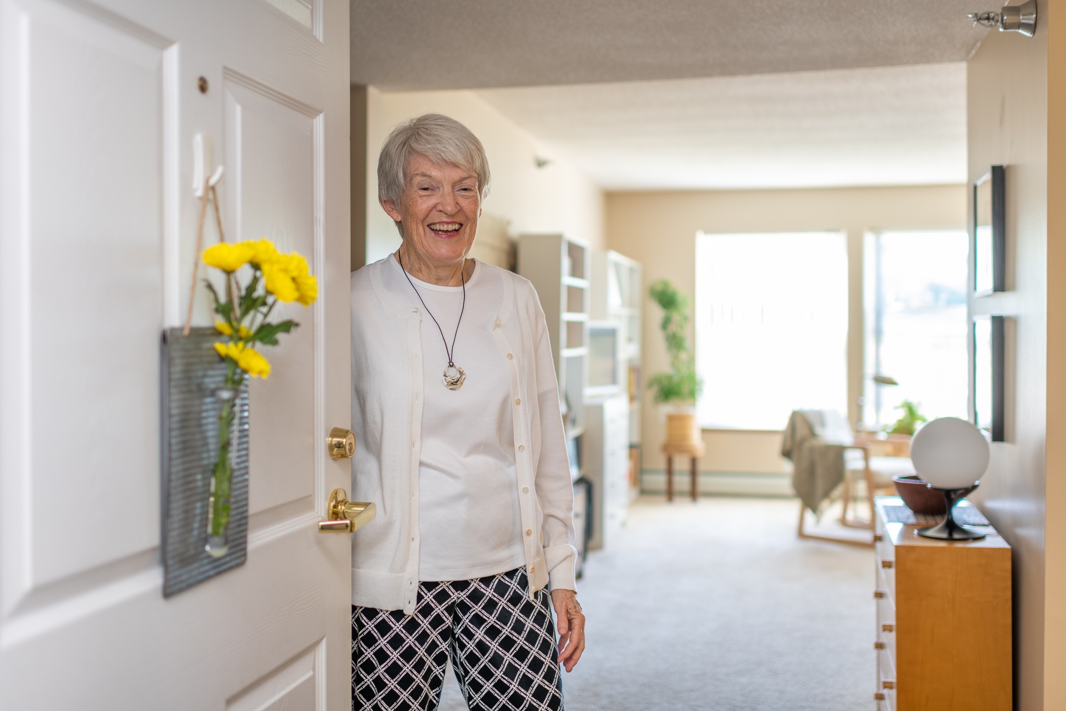 Elderly woman smiling while standing in a sunlit hallway - senior living communities near me